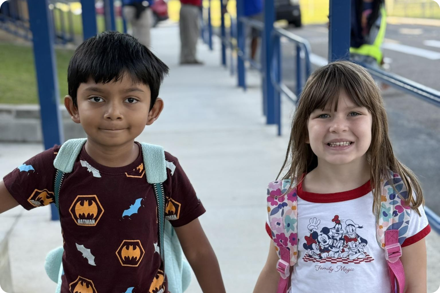 two little kids with backpacks holding hands on a sidewalk